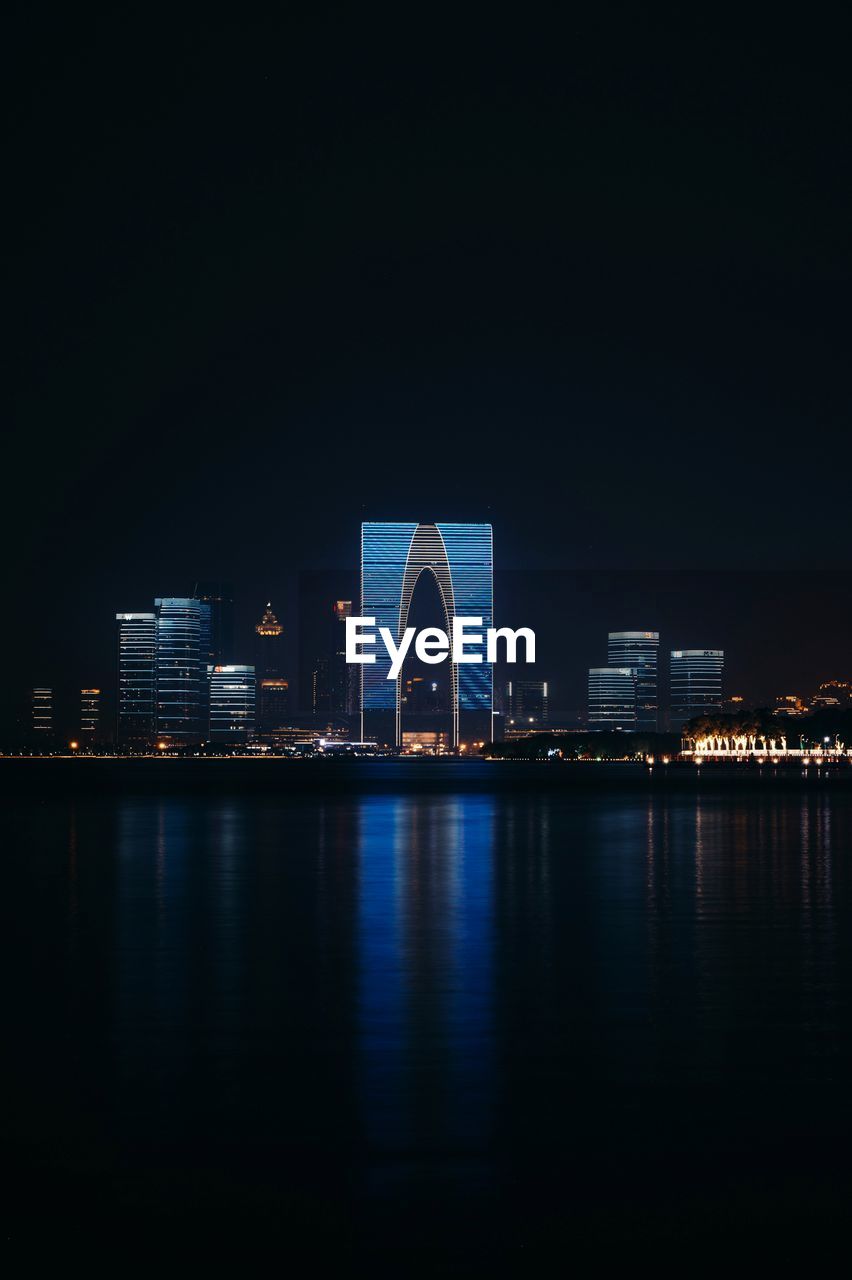 Illuminated buildings by river against sky at night