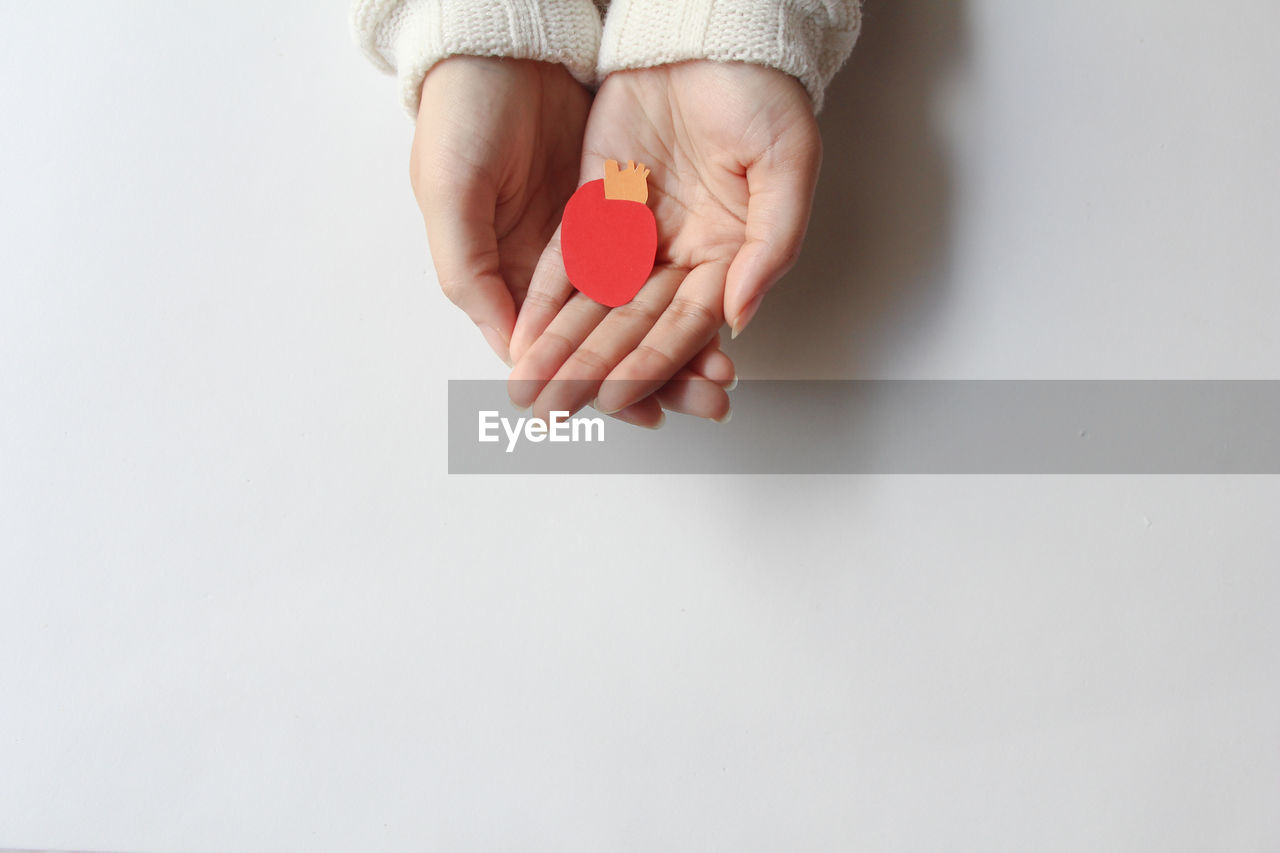 cropped hand of woman holding heart shape on white background