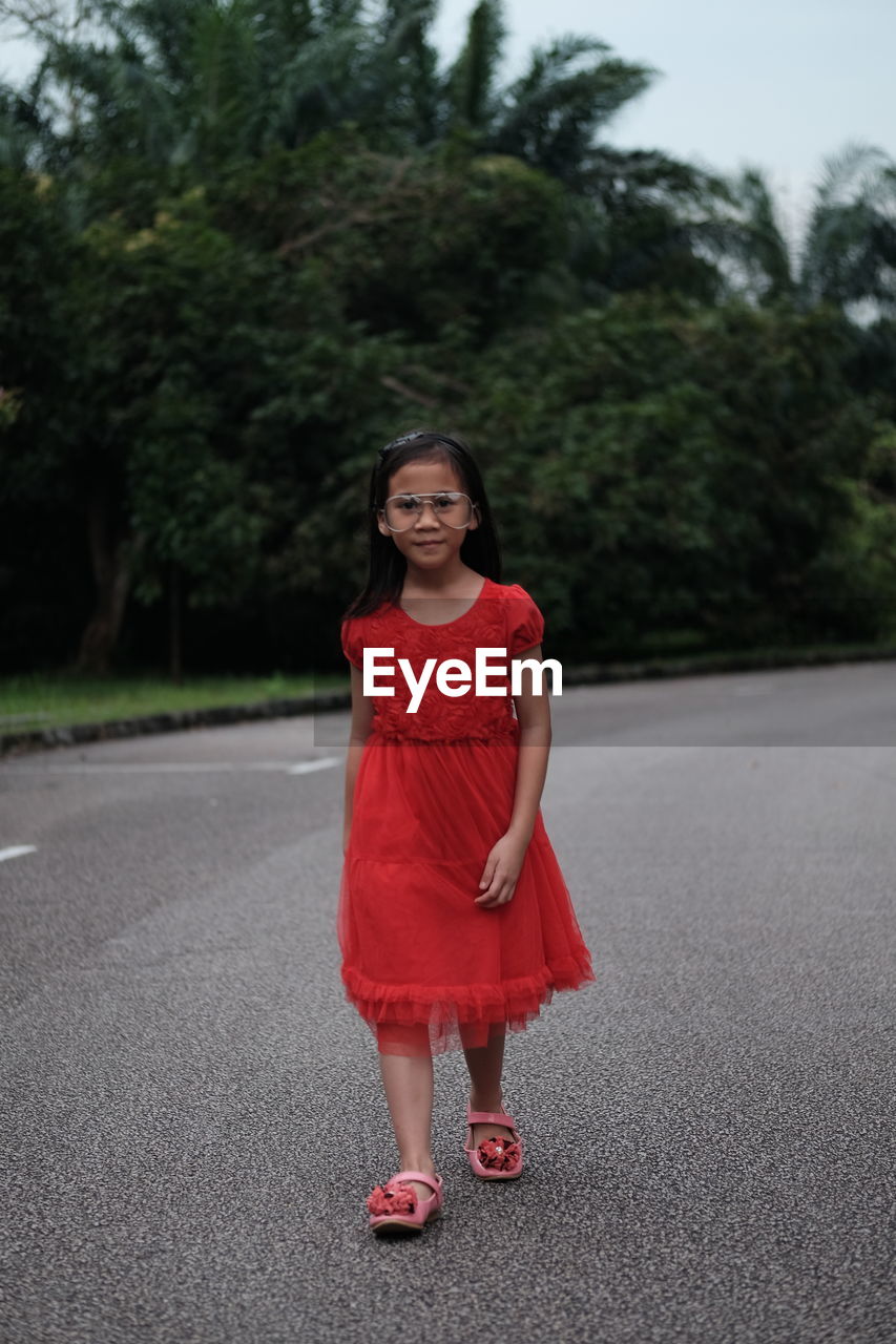 Portrait of cute girl wearing red dress while walking on road