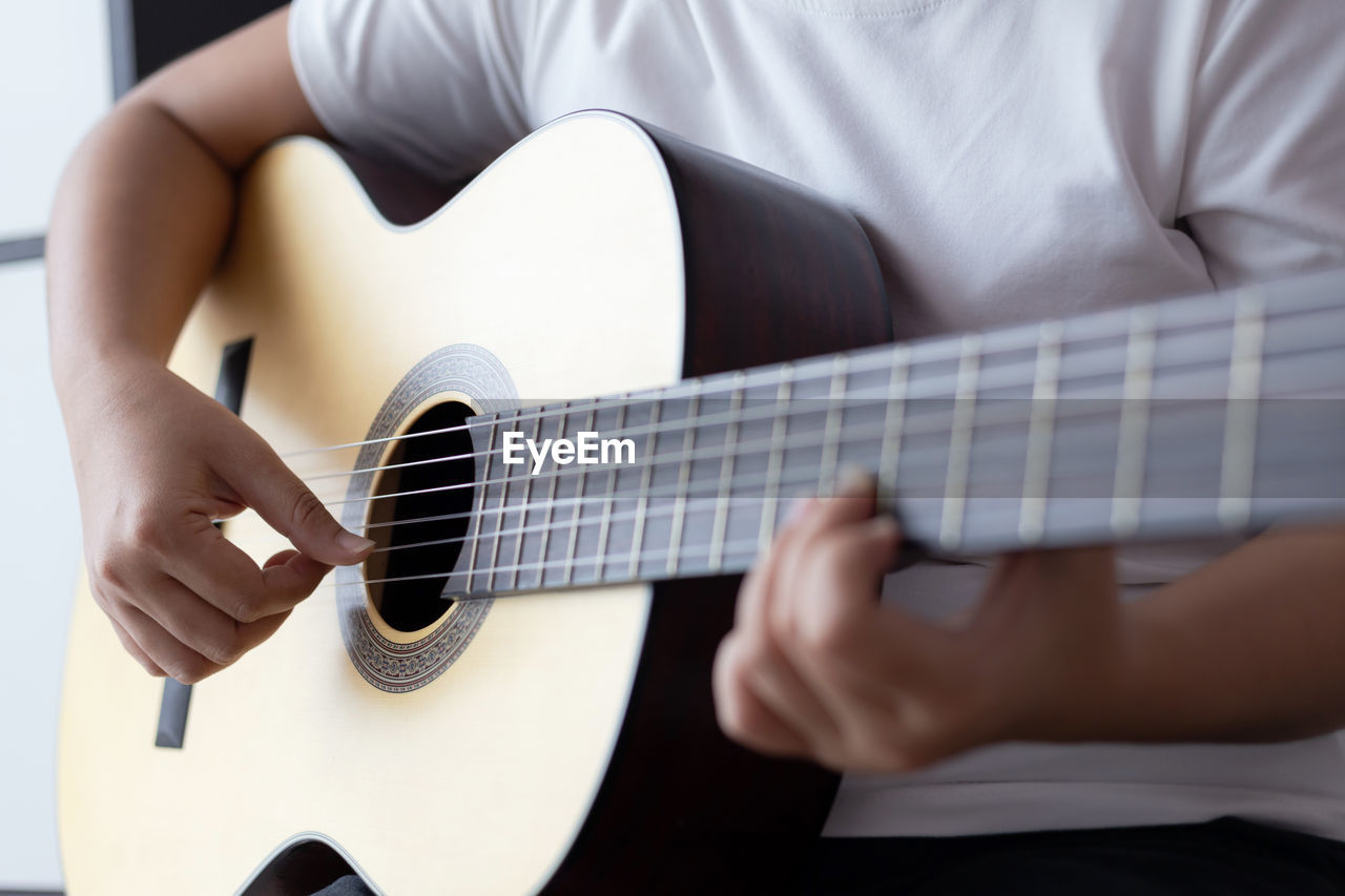 MIDSECTION OF MAN PLAYING GUITAR AT HOME