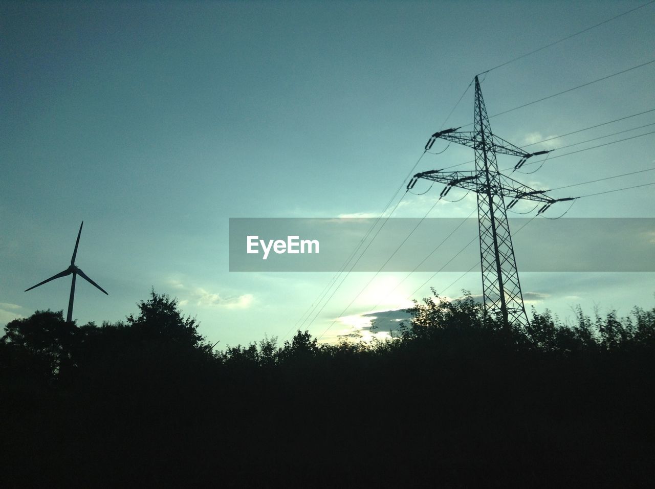 Silhouette of wind turbines and power lines at dusk