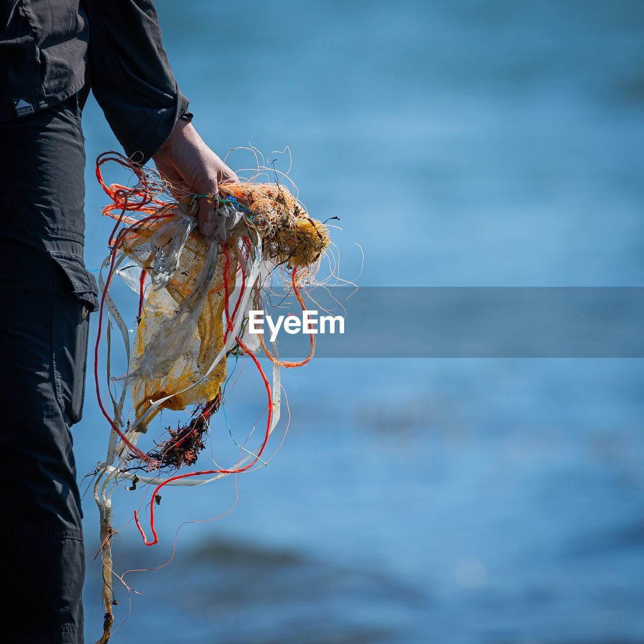 Midsection of person holding fishing net at sea shore