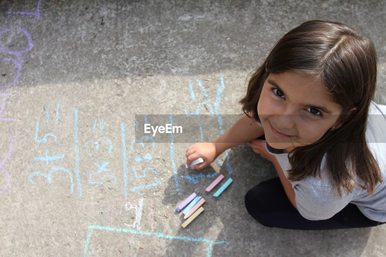 High angle portrait of girl writing with chalk on footpath