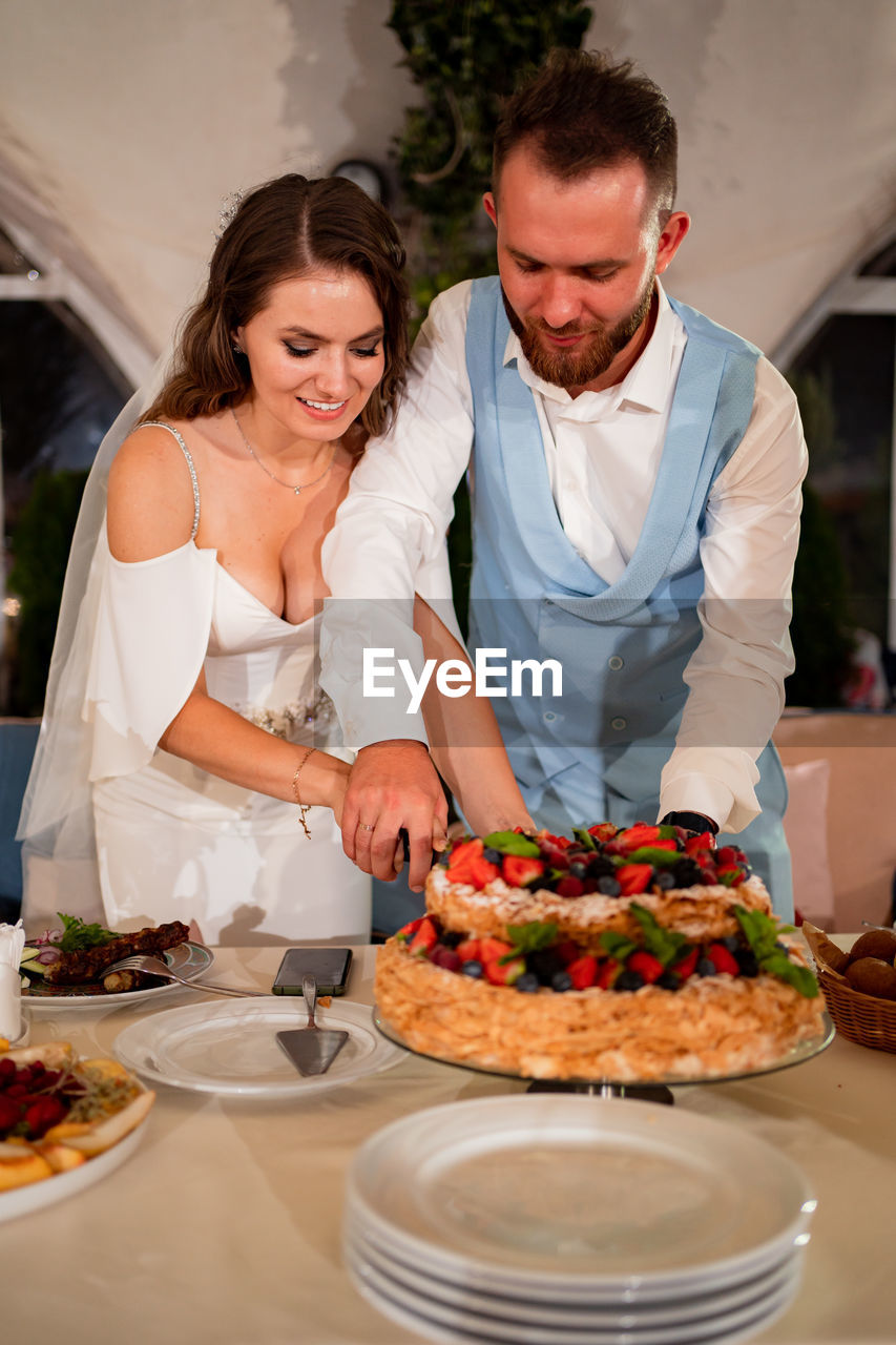 Newlywed couple cutting cake at home