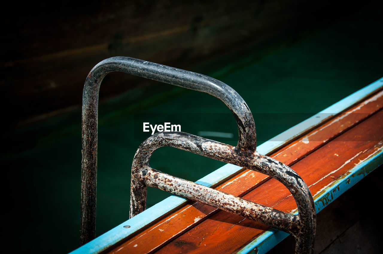 HIGH ANGLE VIEW OF RUSTY METAL RAILING AGAINST WATER