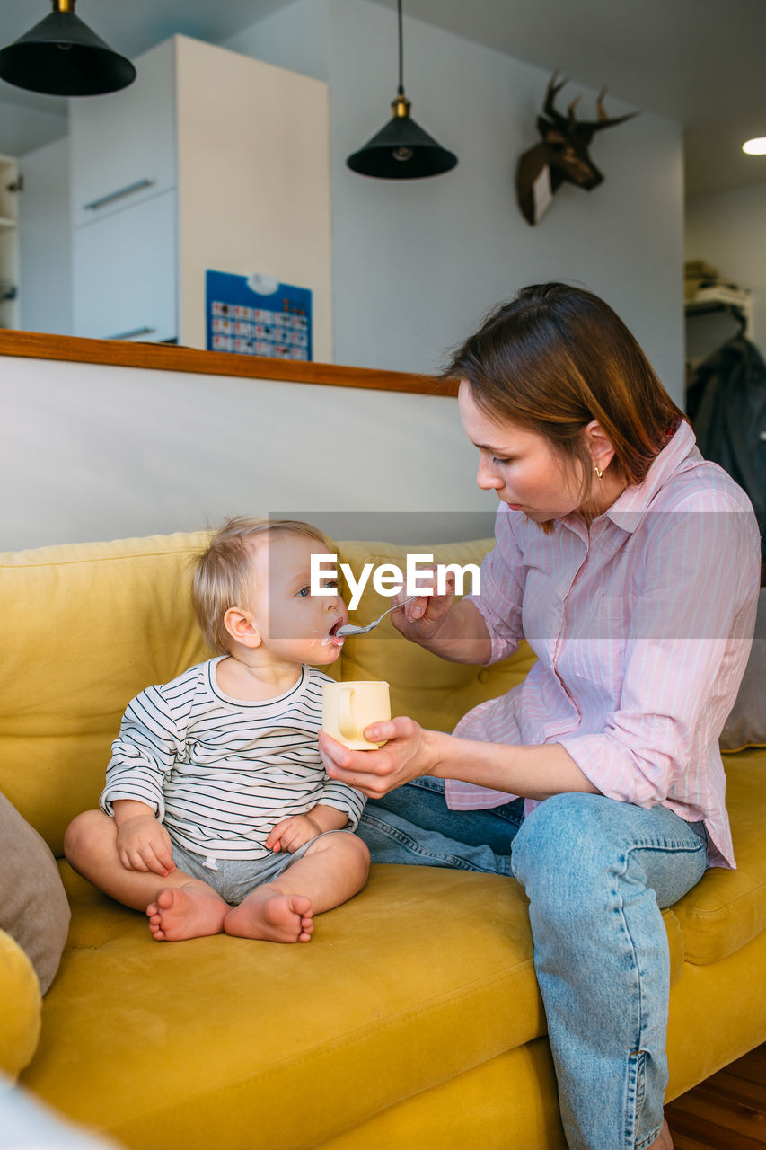 Mom feeds a small child at home with yogurt from a spoon. family concept