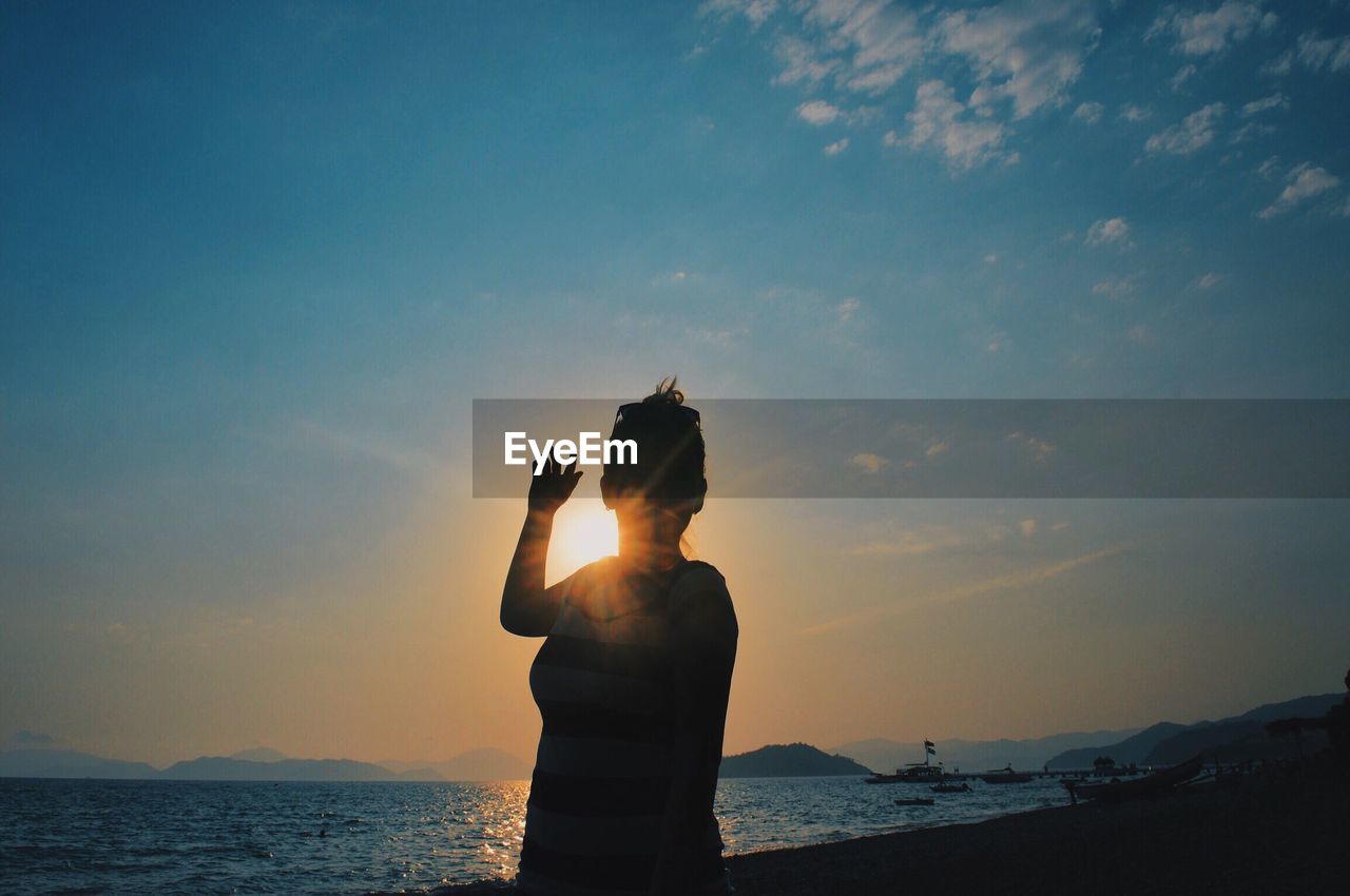 Silhouette woman standing on shore at beach during sunset