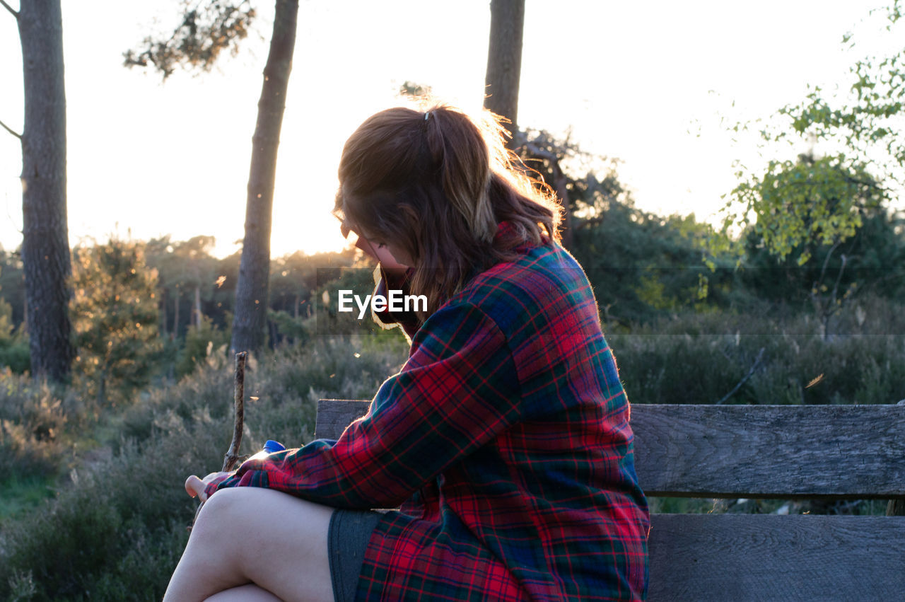 Woman sitting on bench at field against clear sky