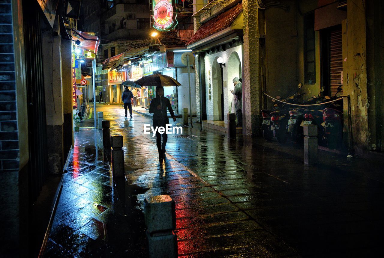 Silhouette woman walking on wet city street at night