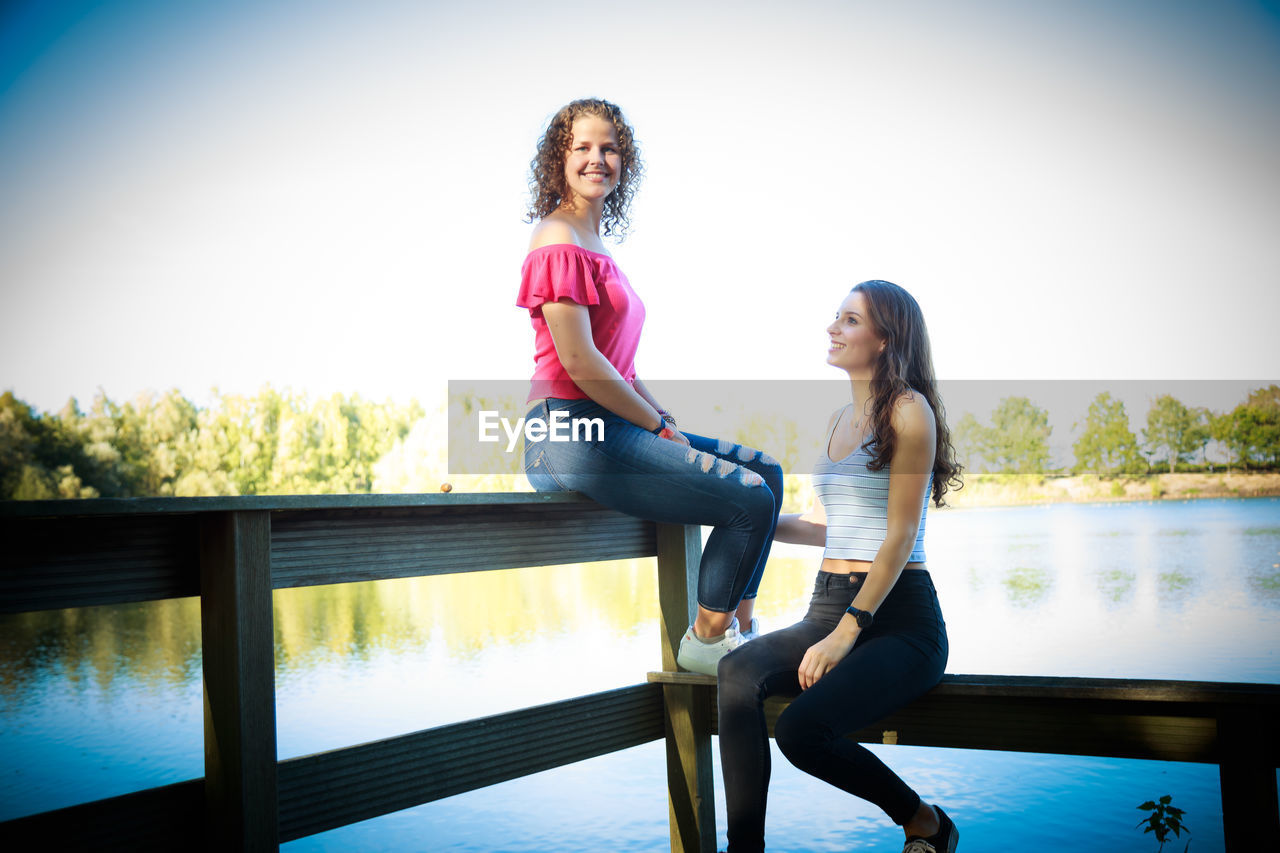 WOMAN SITTING ON RAILING AGAINST SKY