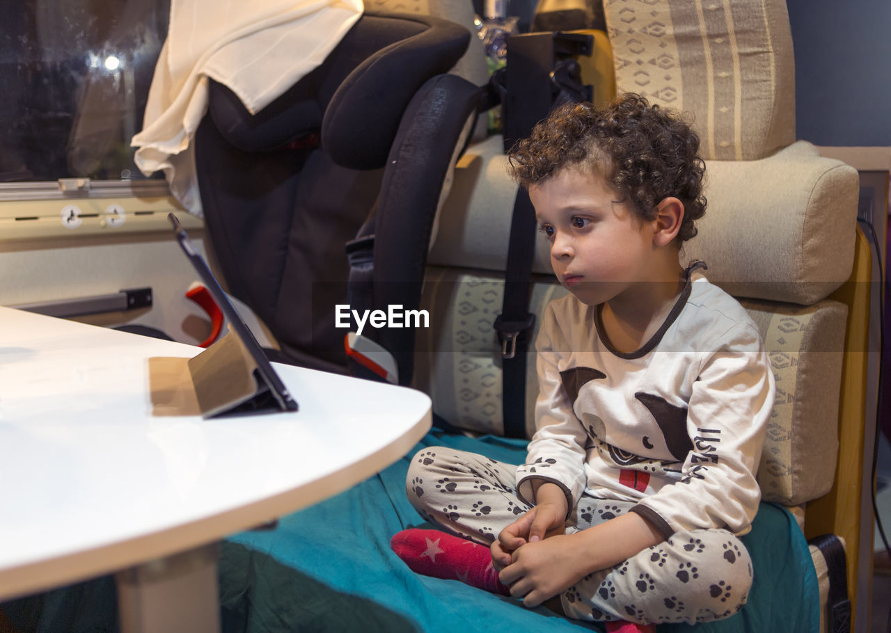  boy inside motorhome entertaining himself by looking at tablet while sitting in pajamas