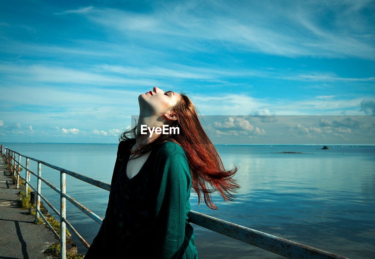 Side view of a woman relaxing on railing by calm sea