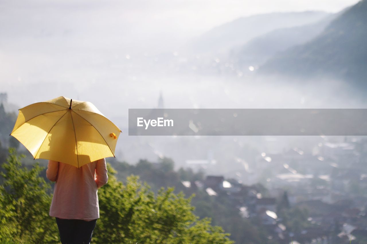 Rear view of woman with umbrella standing against land