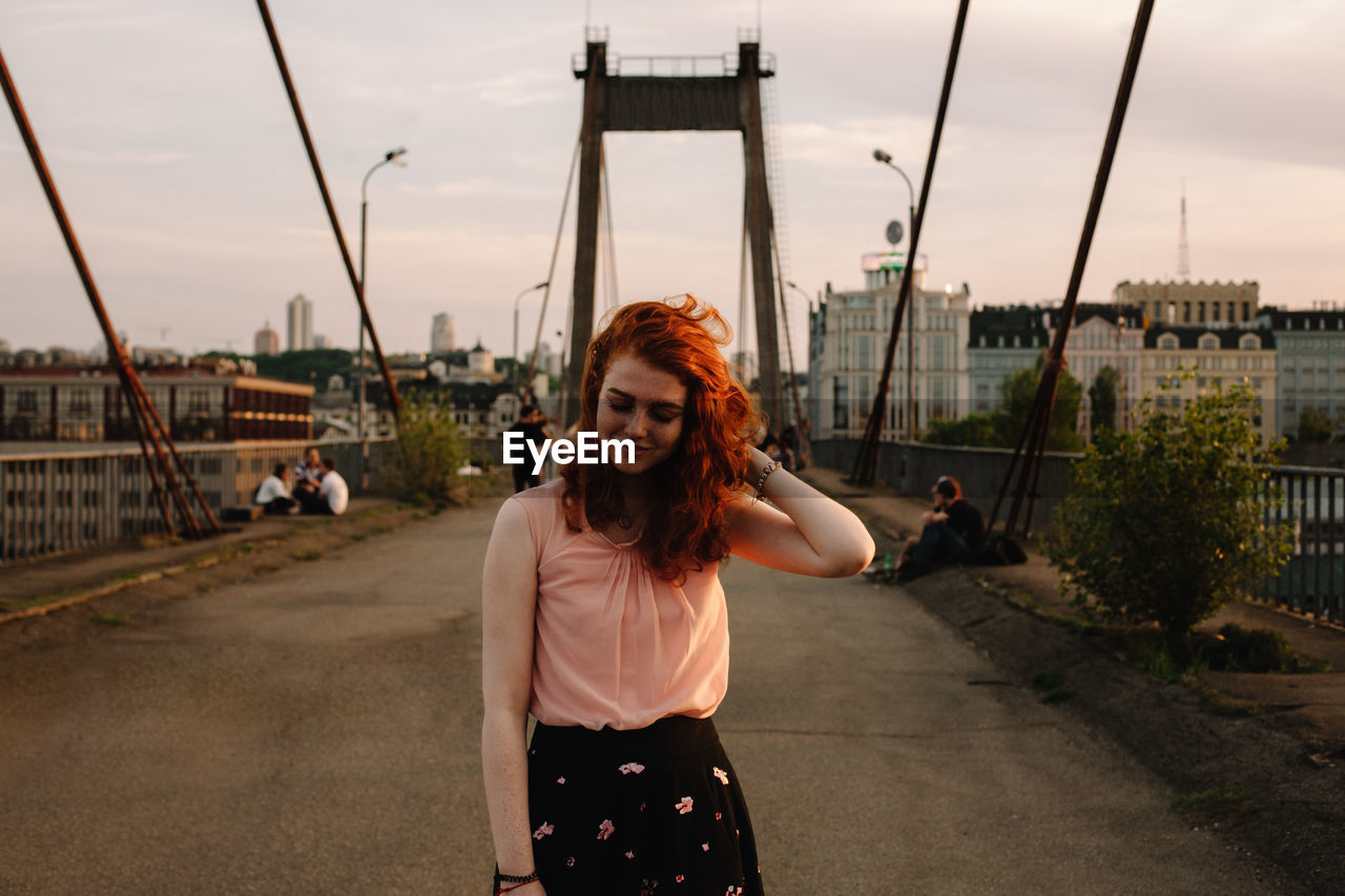 Portrait of smiling redhead woman standing on bridge in city