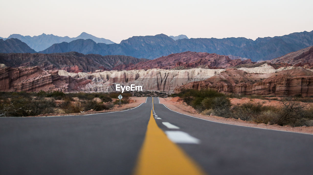 Road leading towards rocky mountains against sky