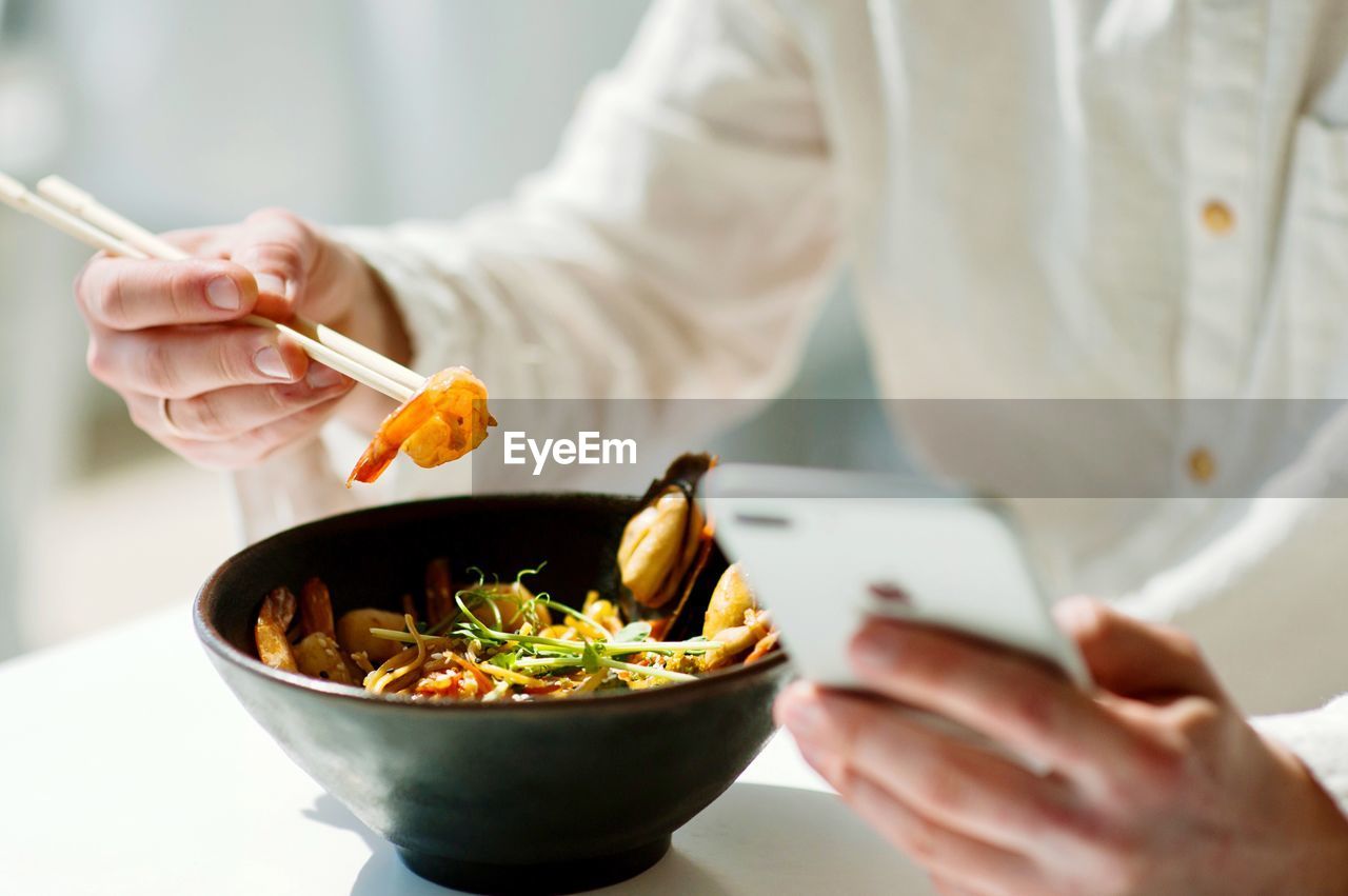 Midsection of person holding food and phone in restaurant