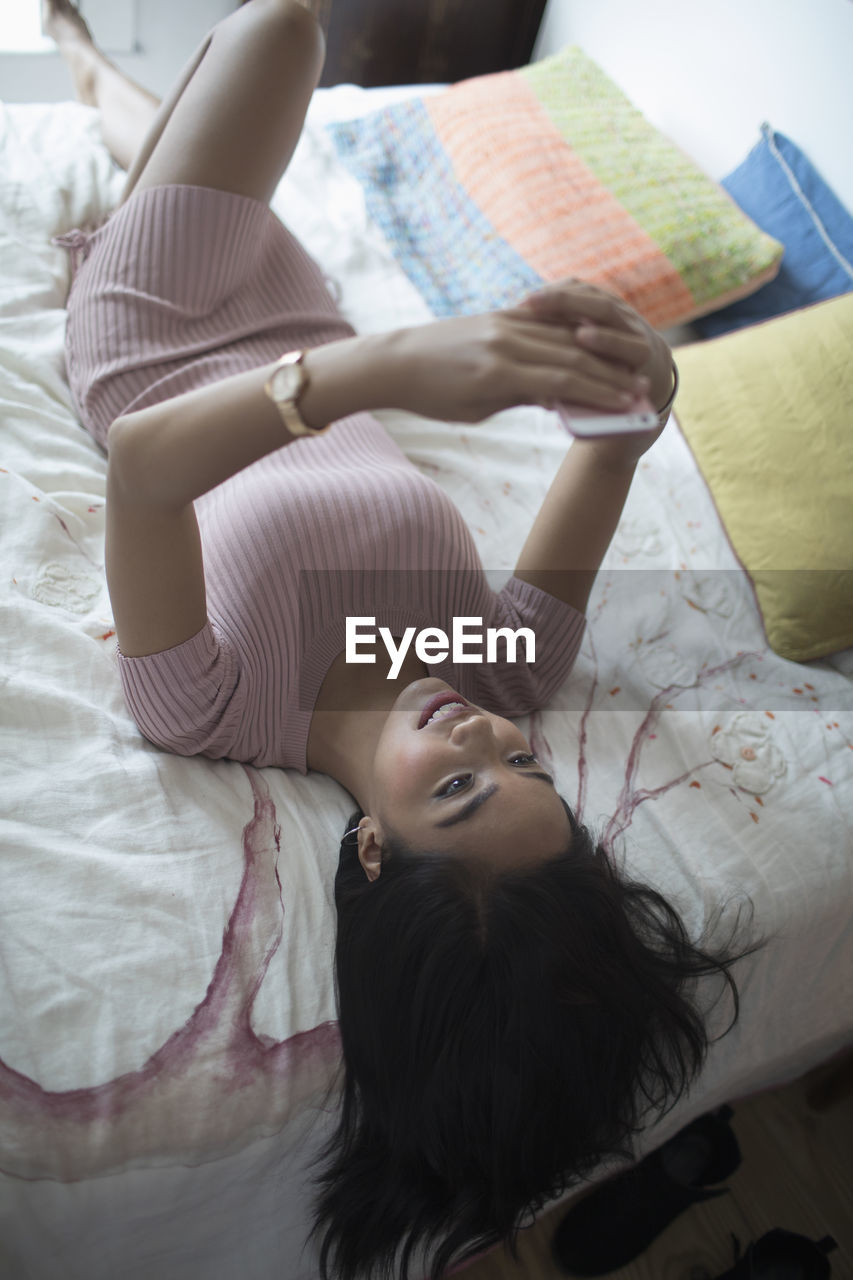 Young woman using her smartphone on her bed