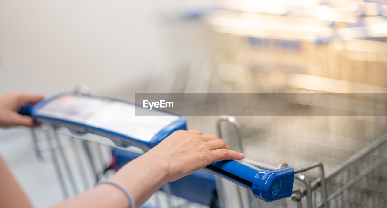 Female hand pushing shopping trolleys in supermarket walking through the aisle