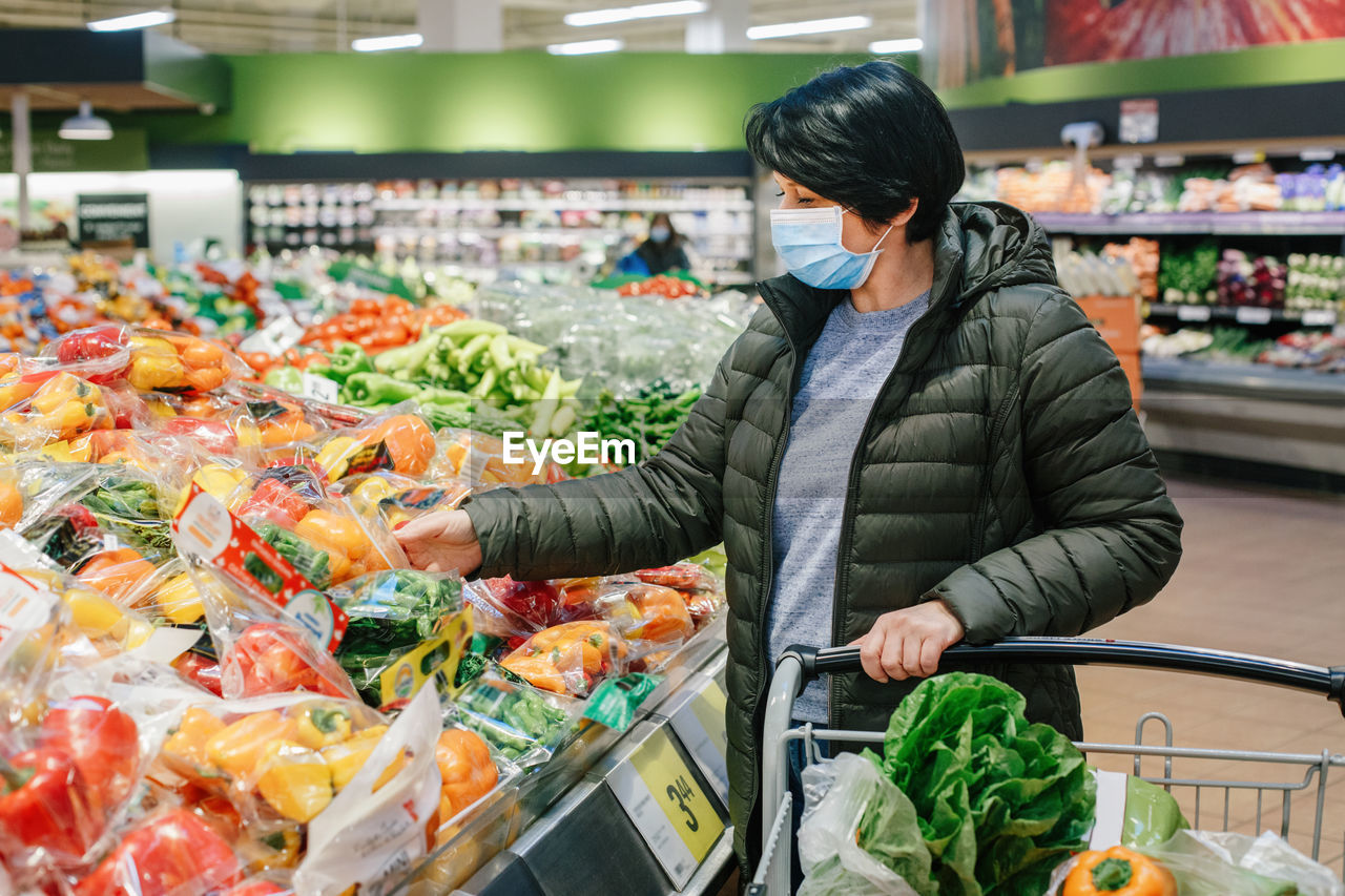 Grocery shopping. middle age woman in protective face mask buying food vegetables in supermarket 