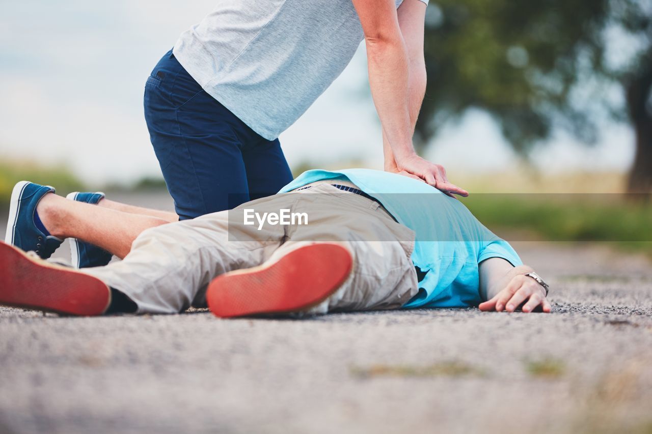 Low section of man resuscitating friend lying on road