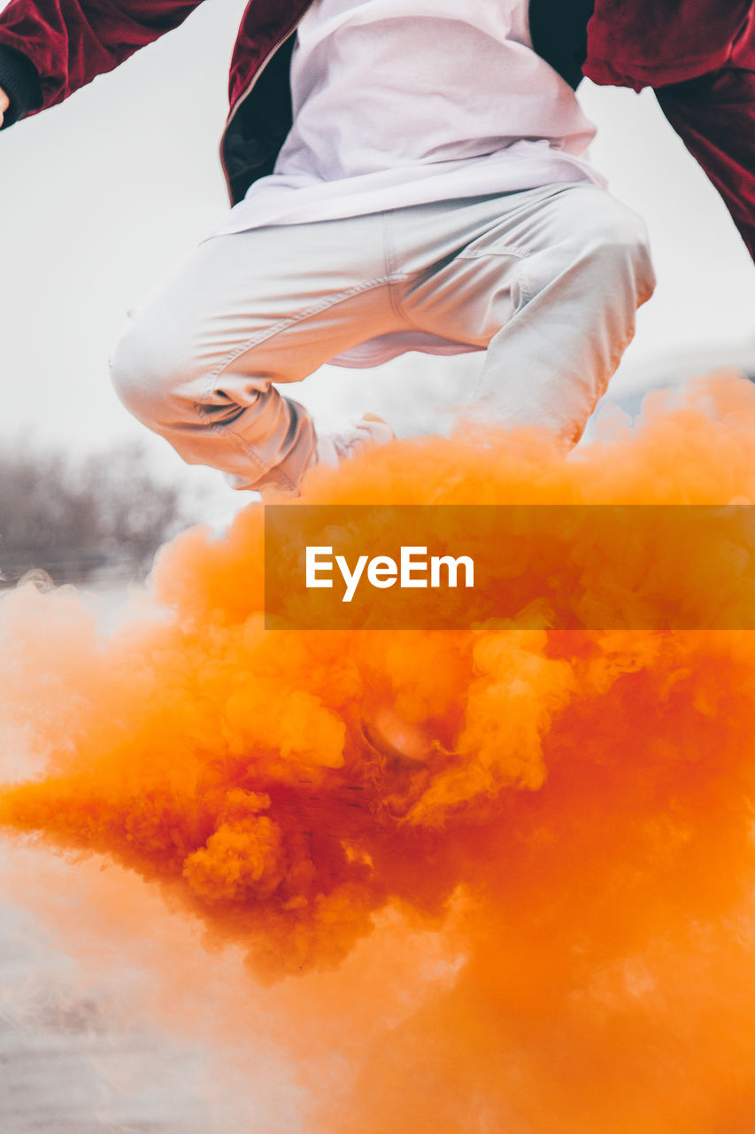 Low angle view of man jumping above orange smoke