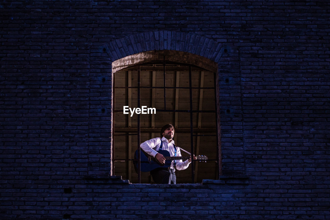 Low angle view of man playing guitar while standing at window