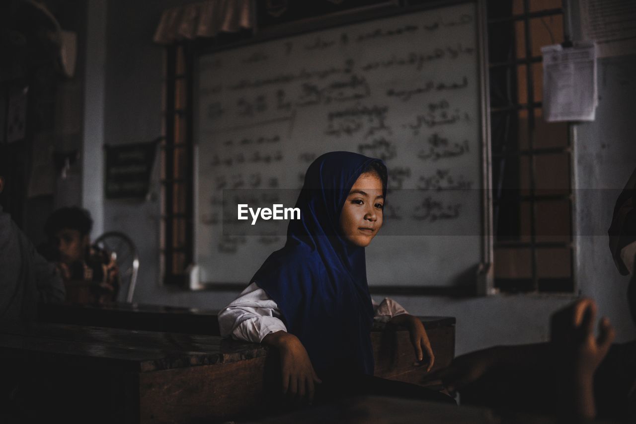 Girl looking away while standing by table with man in background