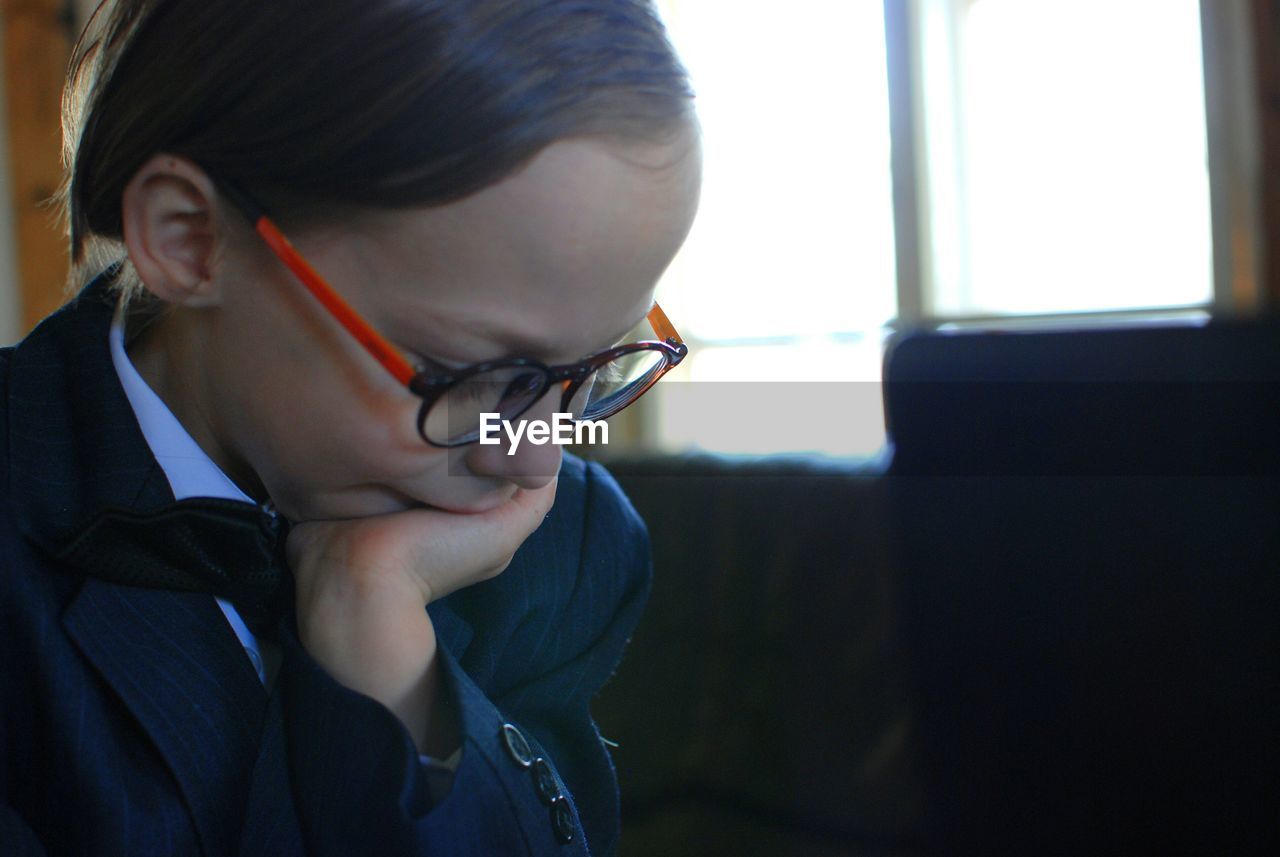 Close-up of boy with hand on chin wearing eyeglasses by brightly lit window