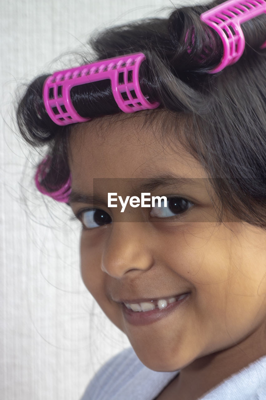 Portrait of girl with hair curlers against wall at home