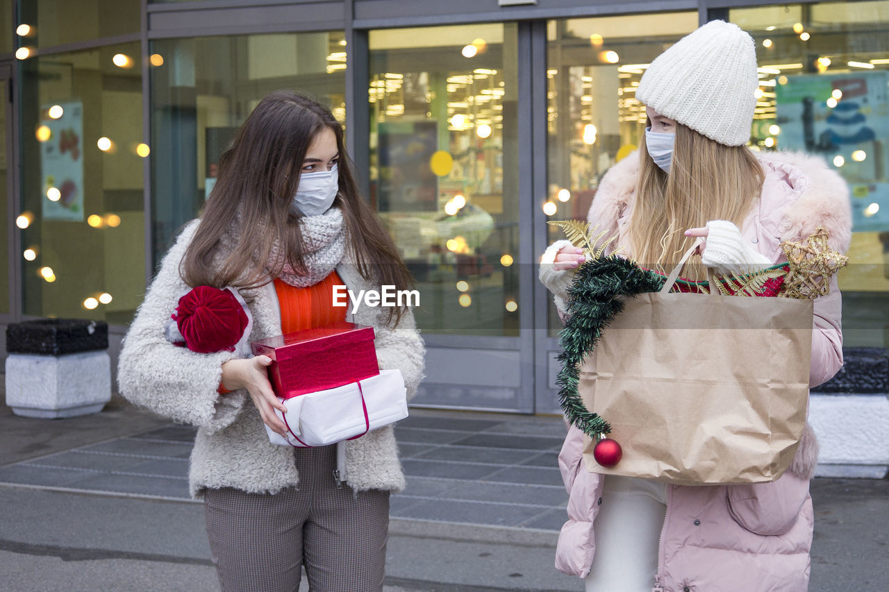 Young women in medical mask shopping for christmas in mall. xmas holidays in new covid-19 reality.