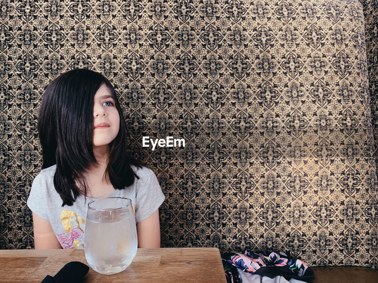 YOUNG WOMAN SITTING ON TABLE AGAINST BRICK WALL