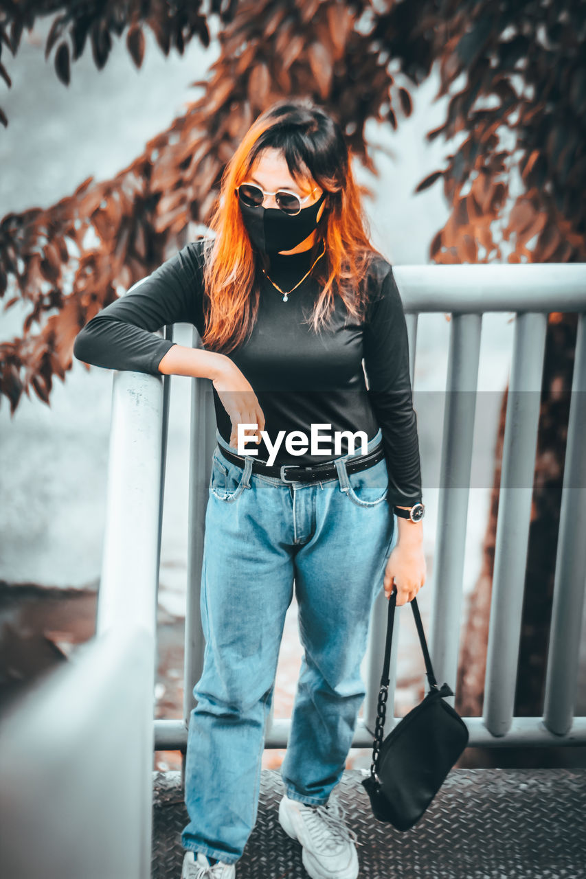 YOUNG WOMAN WEARING SUNGLASSES STANDING ON RAILING