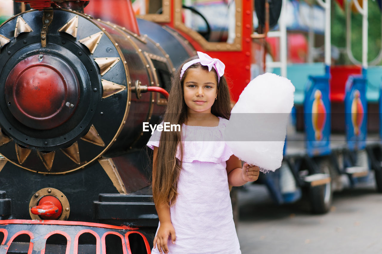 Child girl in an amusement park in the summer eats cotton candy and smiles happily