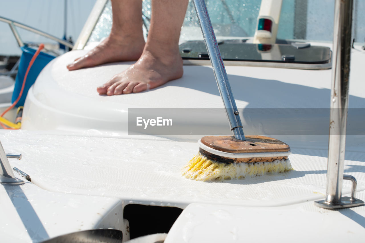 Man washing white boat with brush and pressure water system at pier. yacht maintenance concept.