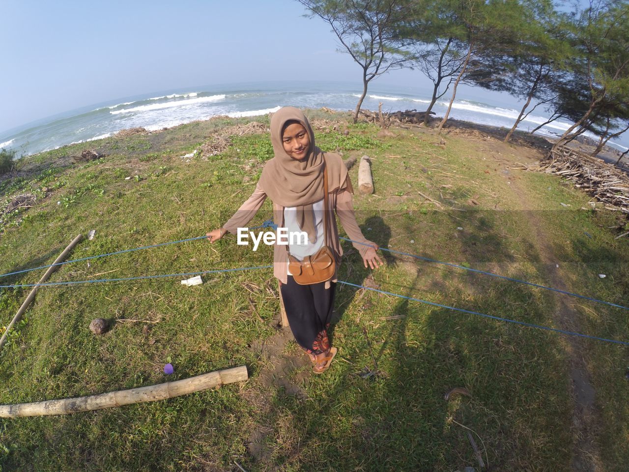 Portrait of young woman standing against sea in sunny day