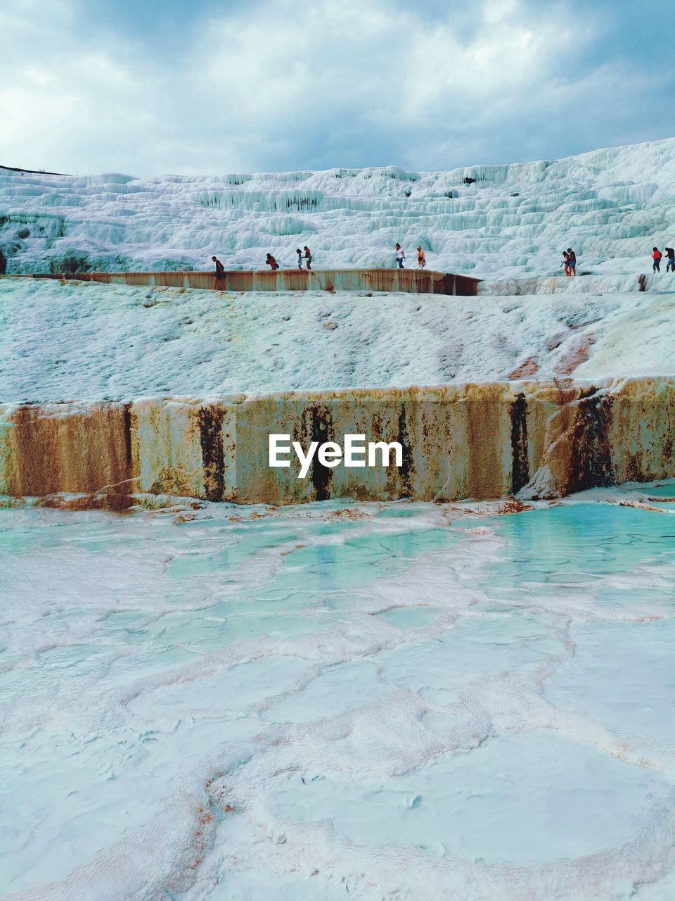 People on travertine pool against sky