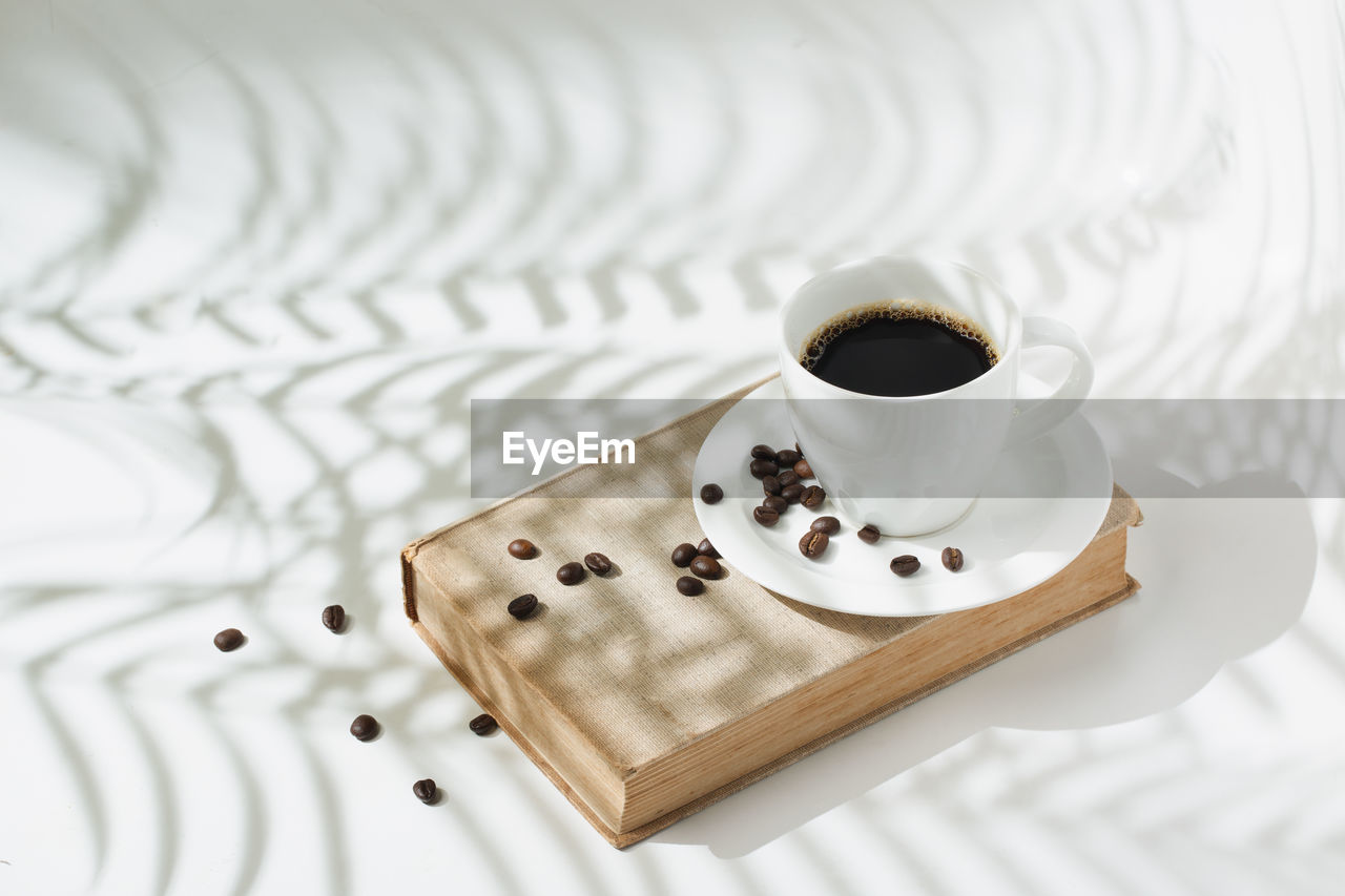 Hot black coffee with coffee beans on modern shadow