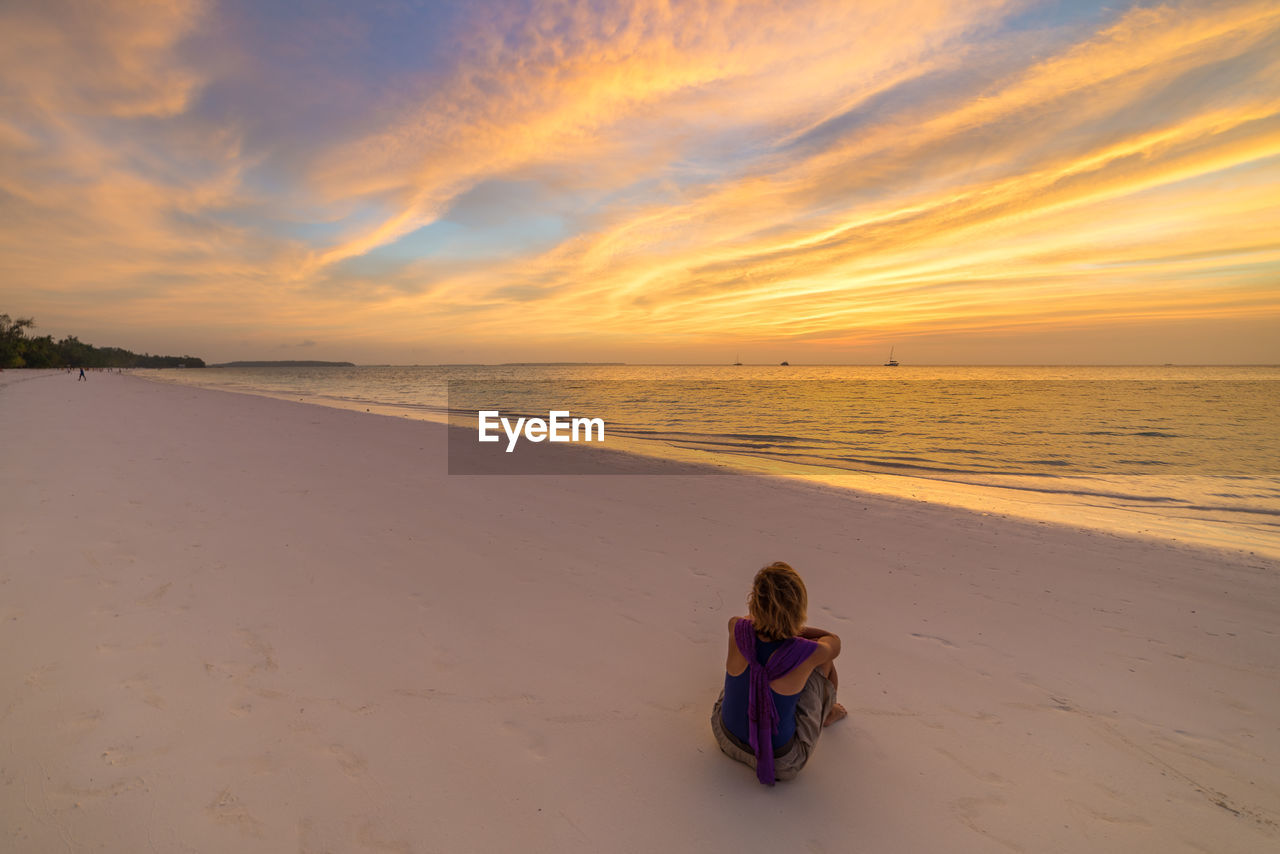 Woman sitting at beach against sky during sunset