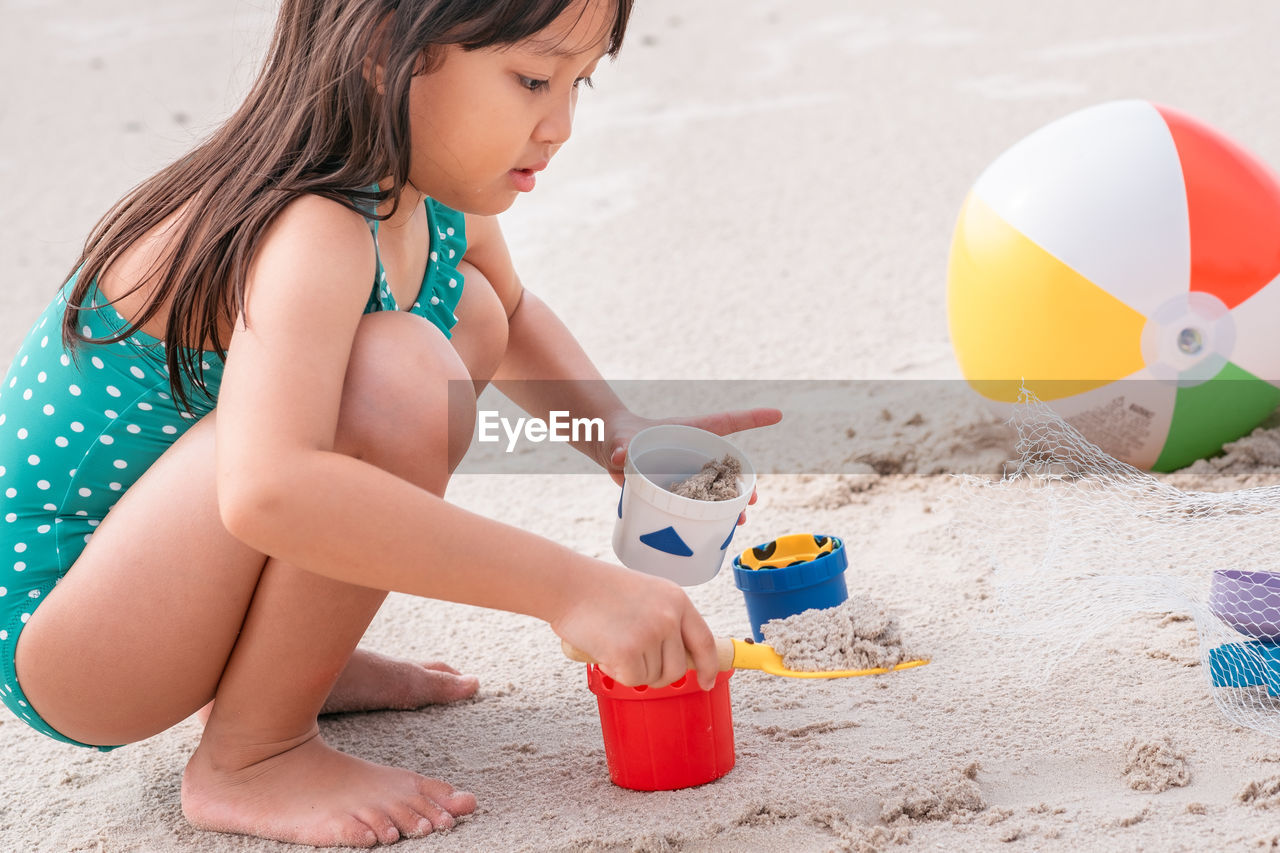 Side view of cute girl in swimwear playing with toys on beach