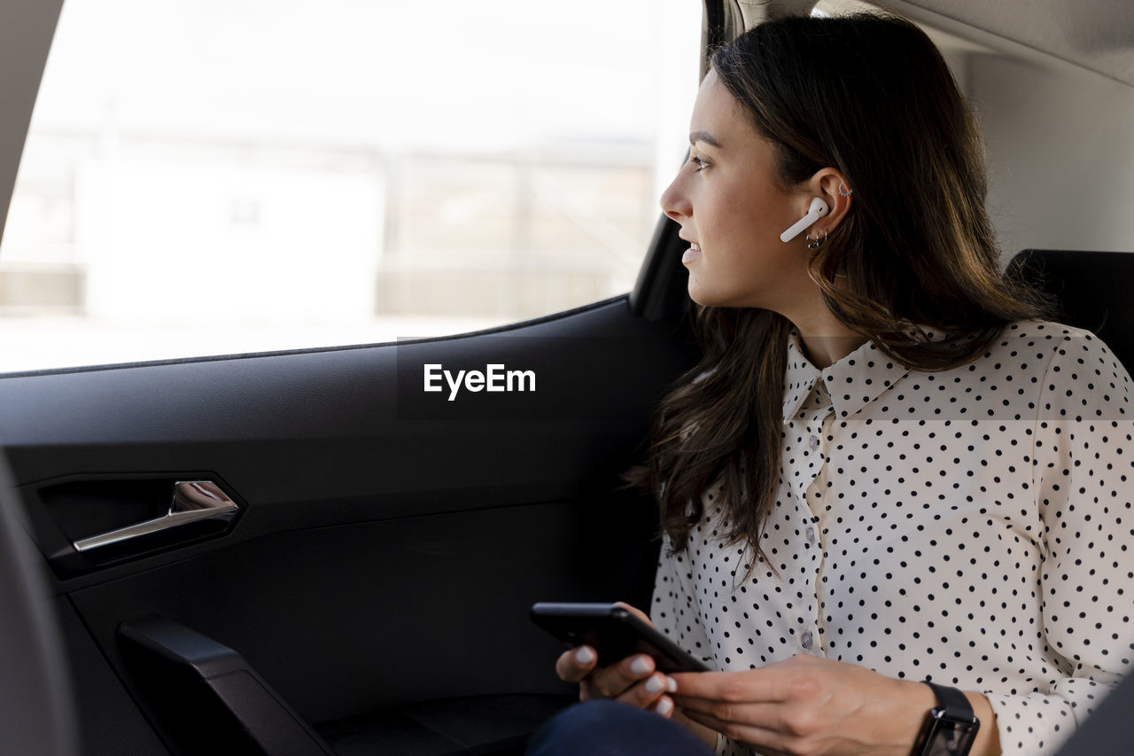 Female professional with wireless technologies looking through window while sitting in car