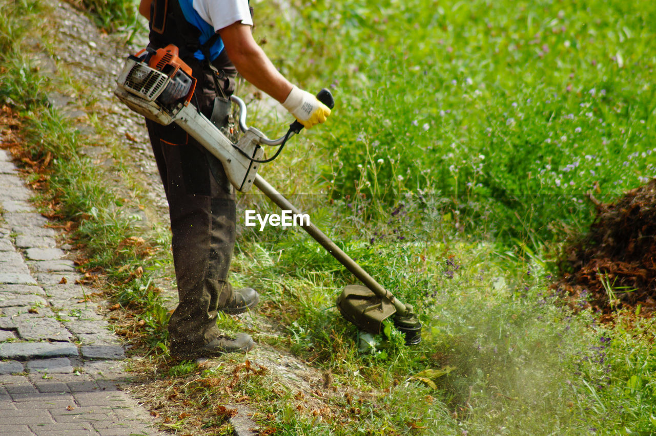 Low section man cutting grass with strimmer in yard