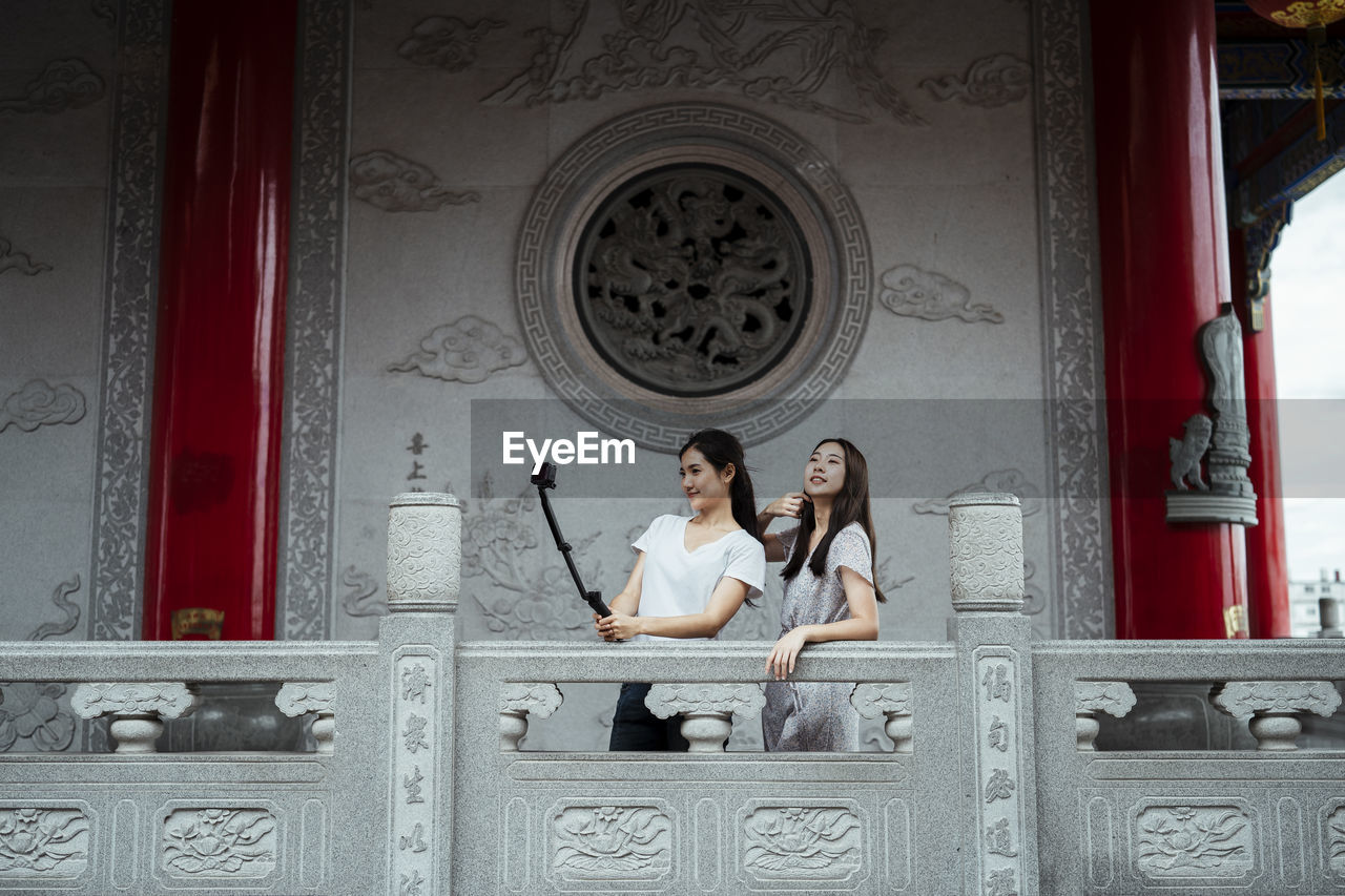 Smiling women embracing while vlogging in corridor