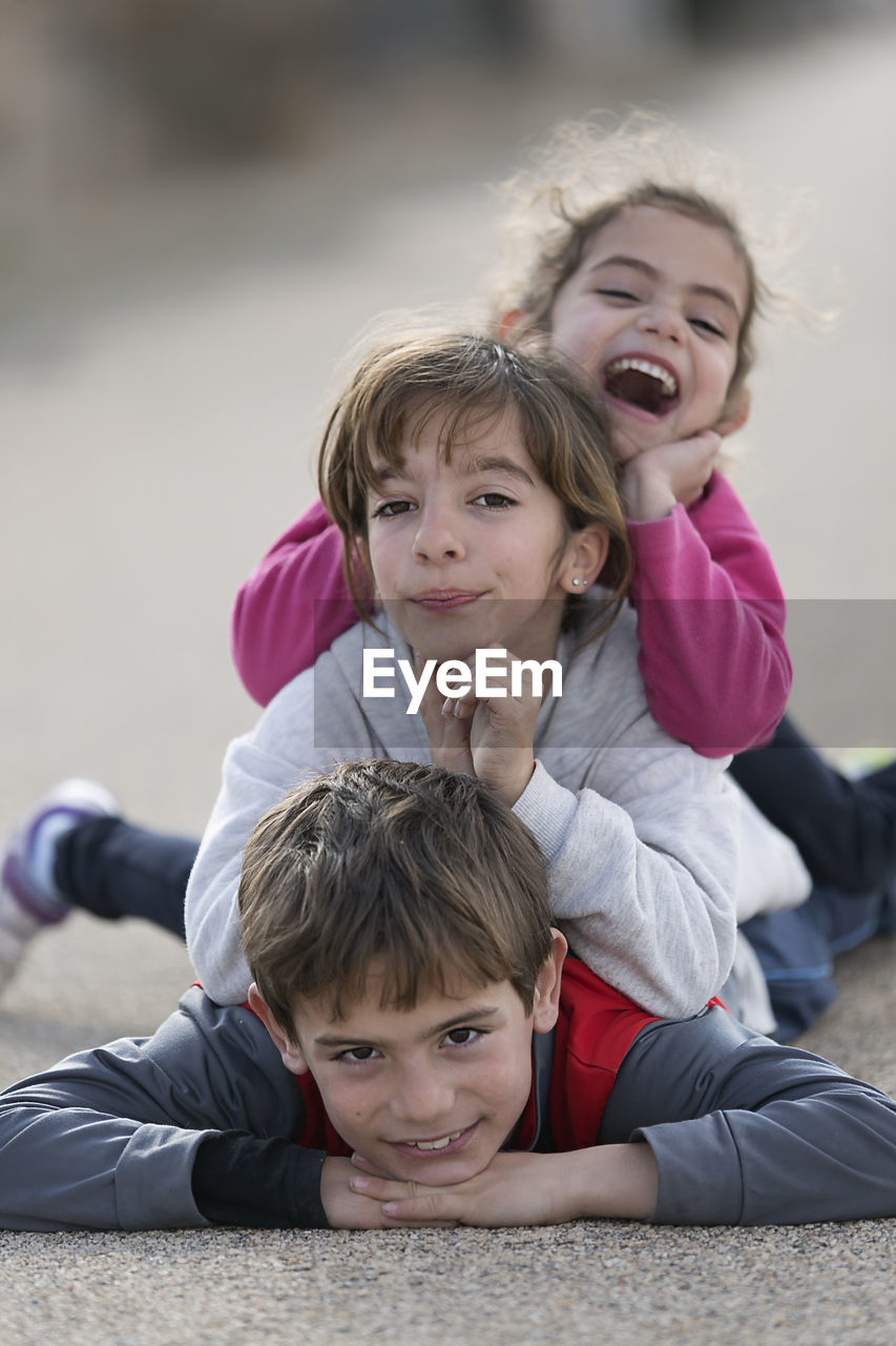 Portrait of boy with sisters lying down on road