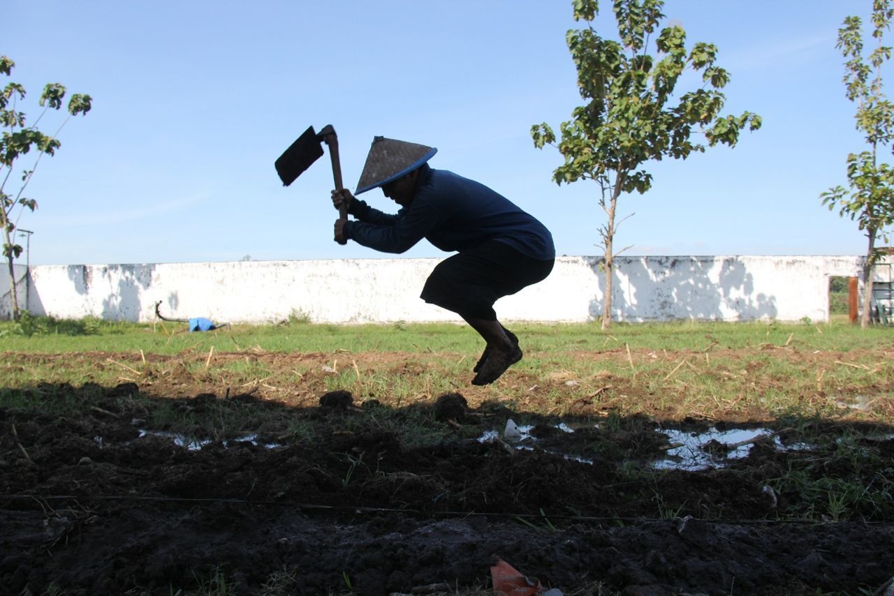 Full length side view of farmer jumping while working in field