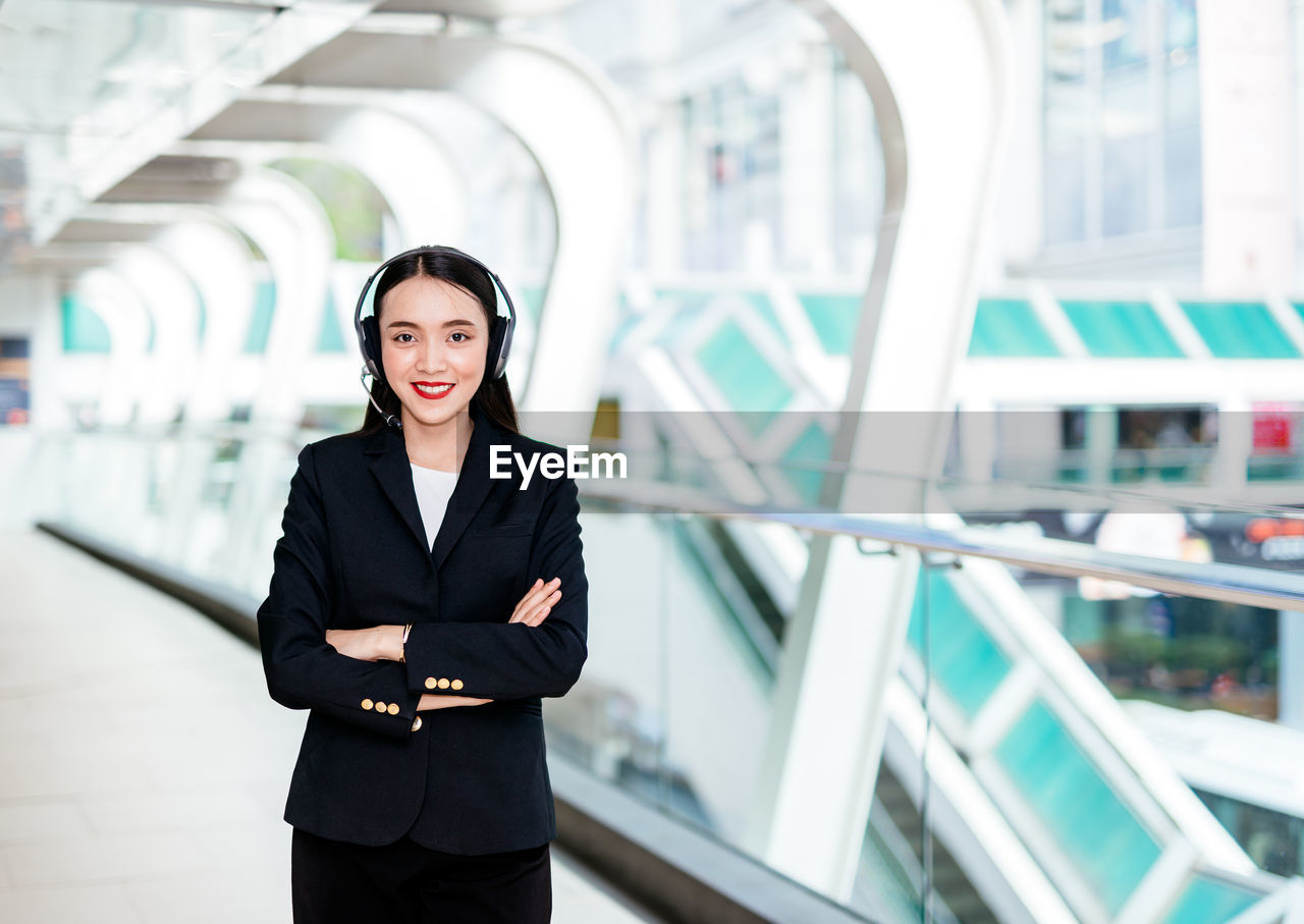 Portrait of smiling businesswoman listening music in corridor