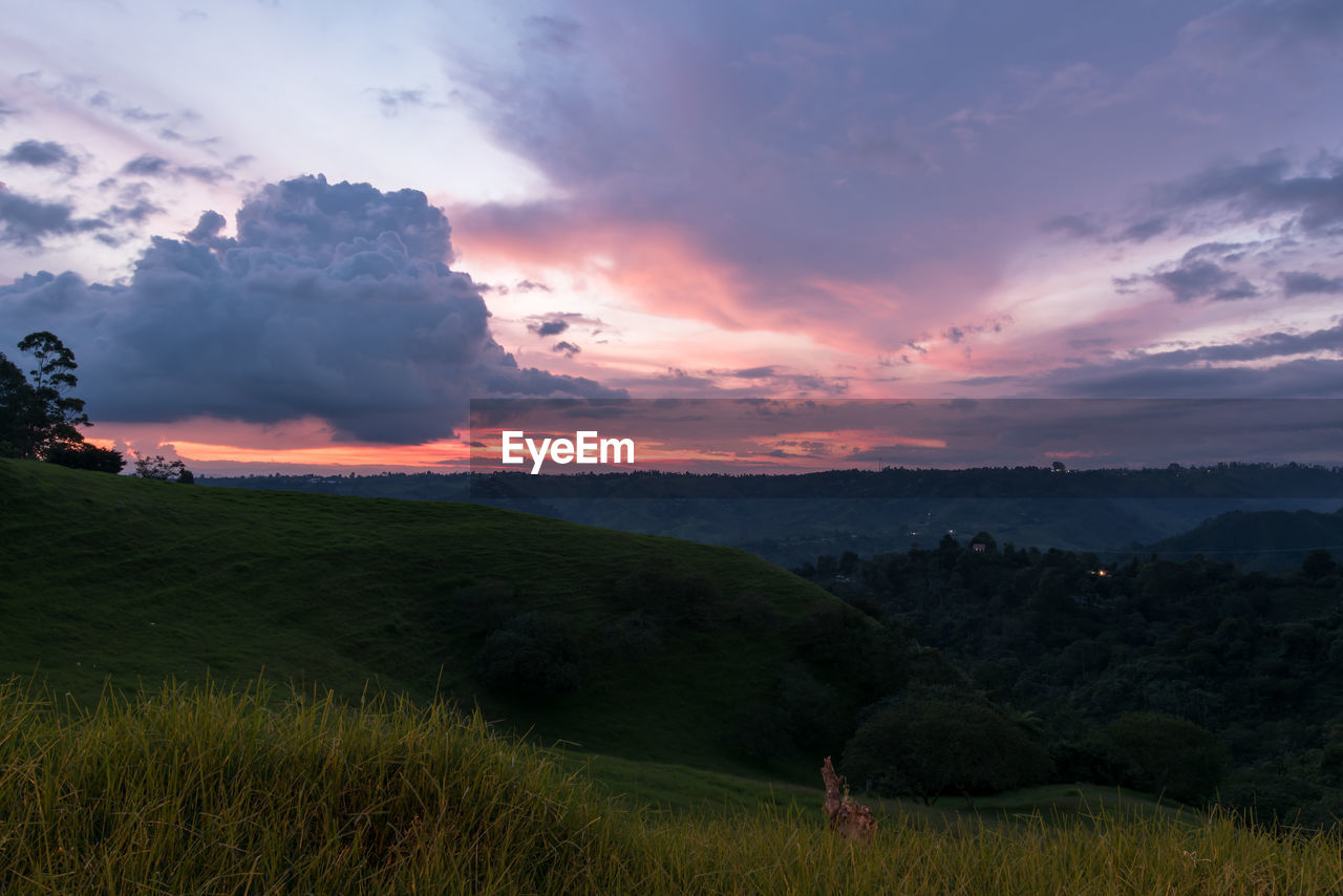 Scenic view of landscape against cloudy sky during sunset