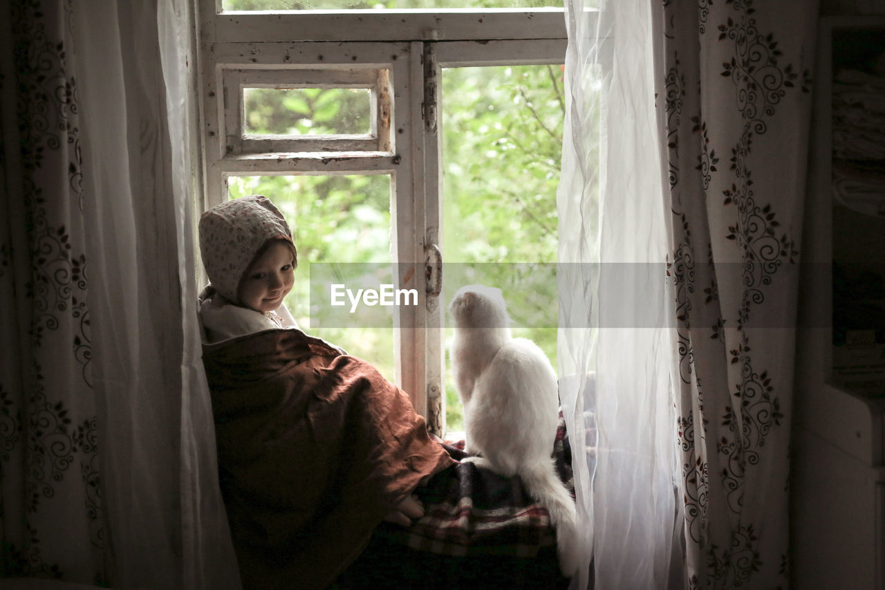 Toddler girl with a cat sitting on the window, concept of a fabulous childhood and favorite animals