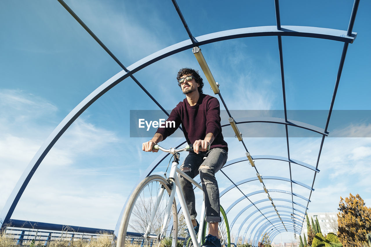 Low angle view of smiling man riding bicycle against sky