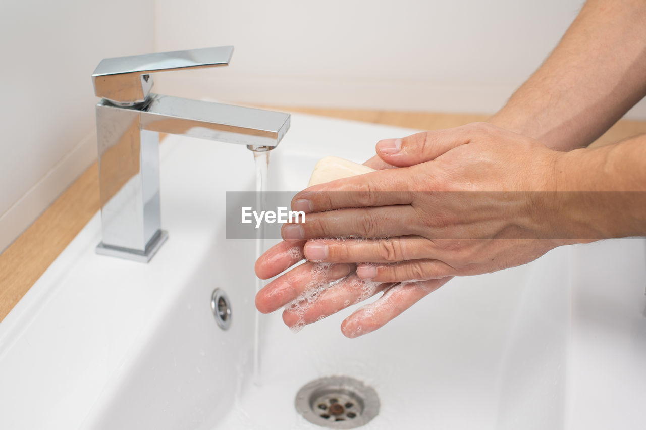 Men's hands with soap under a stream of water in the washbasin