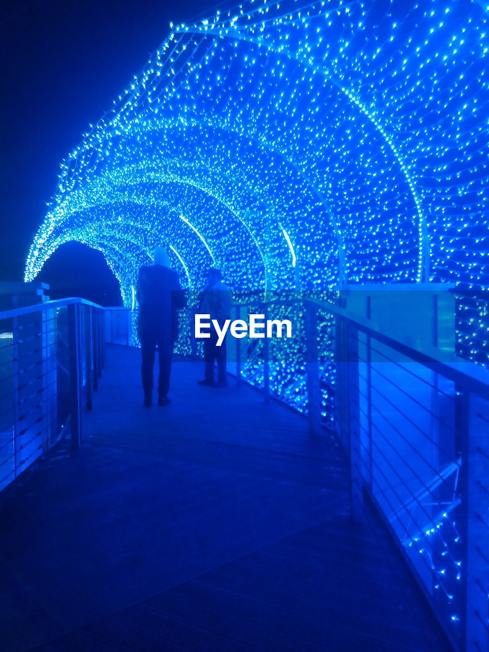 REAR VIEW OF PEOPLE WALKING ON ILLUMINATED STREET LIGHT AT NIGHT